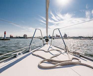 Ein Segelboot fährt im Sommer über ein Gewässer nahe einer Stadt 