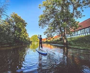 Ein Hotelgast fährt im Wassersporturlaub mit einem Stand Up Board auf dem Fluss 